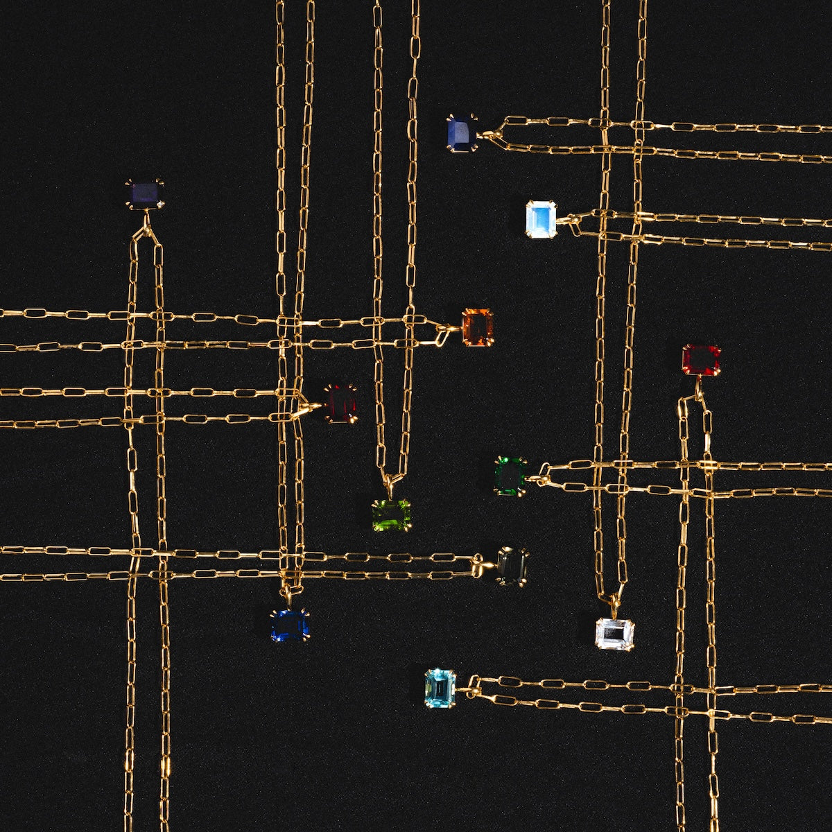 Born to Shine Birthstone Necklaces with gold paperclip chains and colorful rectangular gemstone pendants are arranged in a grid, creating a stylish birthstone display against a black background.