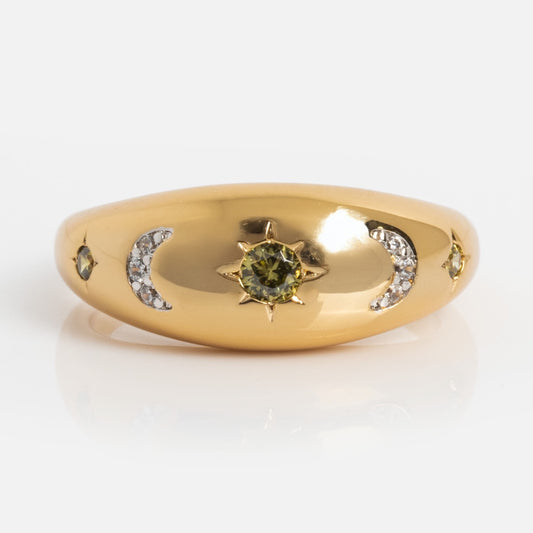 The Moonstruck Bold Dome Ring features a central green gemstone in a star design, flanked by crescent moons with diamonds and smaller green gems—crafted in 14k gold plating, it exudes cosmic elegance.