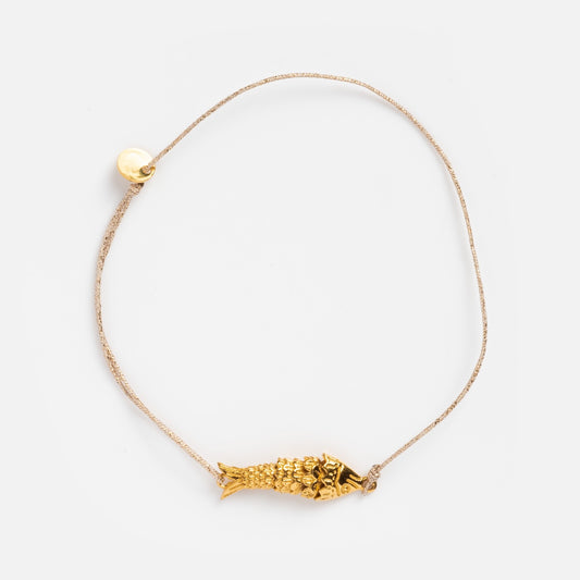 The Sardina Bracelet by Sophie Deschamps Bijoux showcases a thin light cord with a detailed gold fish charm and a small round gold bead, displayed on a plain white background.