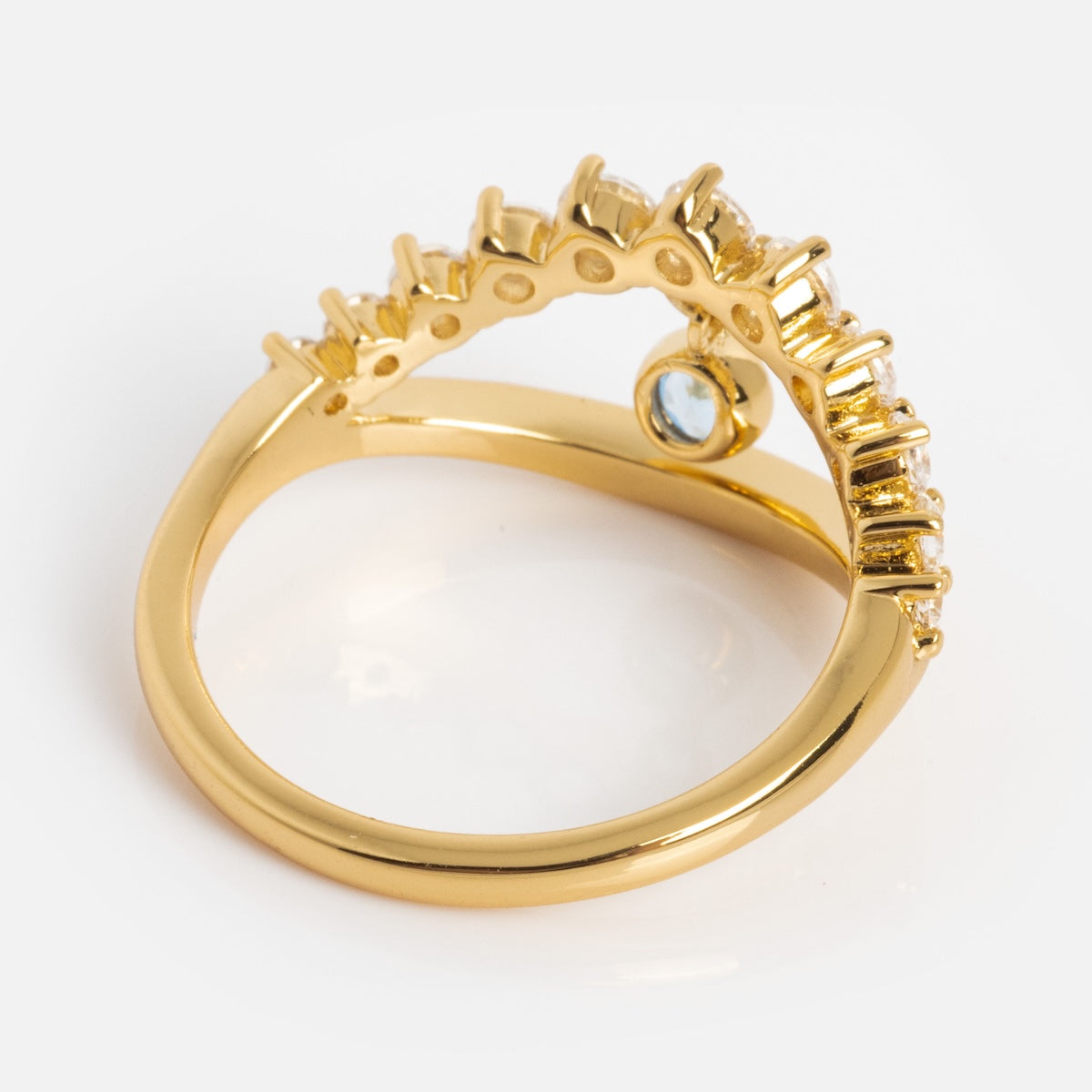 The Mystique Evil Eye Charm Ring features a 14k yellow gold-plated curved band with sparkling gems on top and a single round blue gemstone on the inner side, shown against a white background.