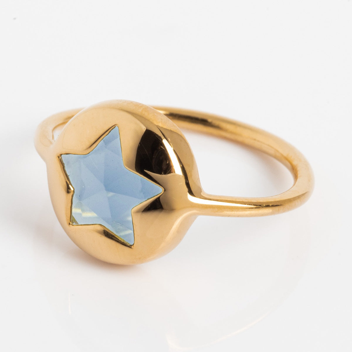 The Maomi Ring is a yellow gold plated ring with a round, slightly raised setting and a star-shaped, faceted London blue topaz gemstone at the center, shown on a white background.