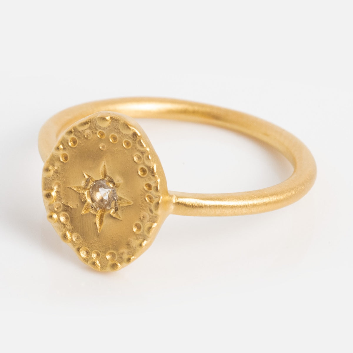 The Brahma Ring features yellow gold plating, a textured irregular round face with a central white topaz gemstone, and decorative dotted patterns around the edge, shown on a plain white background.