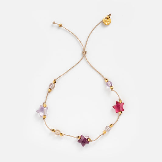 The Martha Bracelet features delicate gold-plated beads, five star-shaped beads in pink, purple, and clear tones, plus a gold charm with an engraved design at the end. Its adjustable for the perfect fit and adds a touch of elegance to any look.