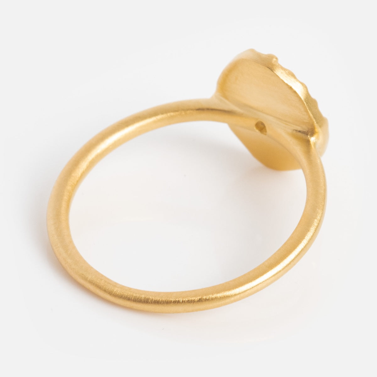 The Brahma Ring, featuring a yellow gold plated, textured oval bezel setting, is shown from an angle that highlights its smooth matte finish and simple, elegant band.