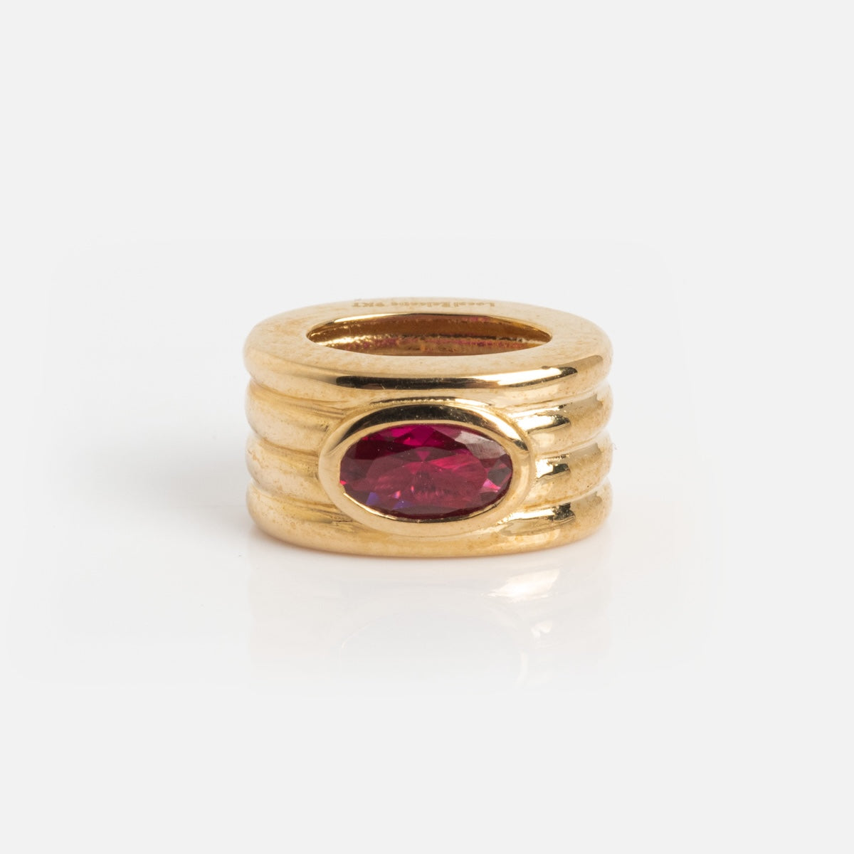 The Solid Gold Bold Birthstone Spacer Charm features a cylindrical design with three horizontal grooves and a central oval red gemstone, shown against a plain white background.