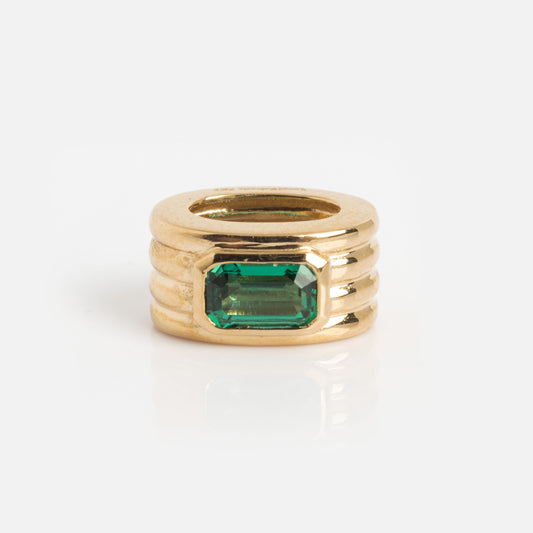 The Solid Gold Bold Birthstone Spacer Charm is a chunky gold ring featuring three horizontal ridges and a rectangular green gemstone in the center, displayed against a plain white background.