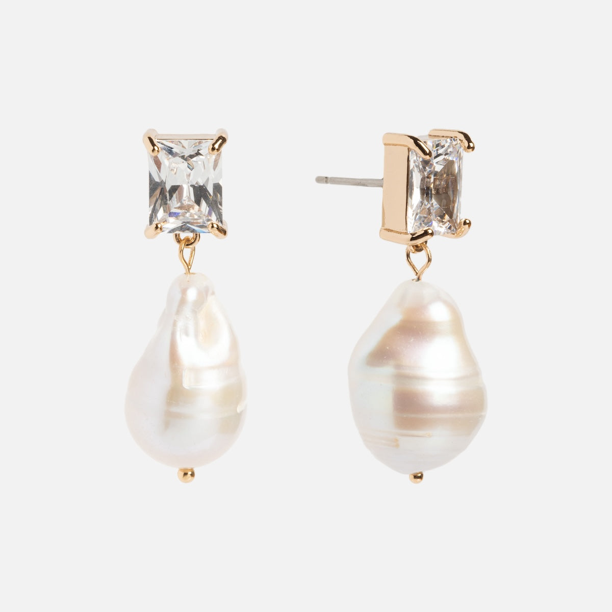 The Zeta Drop Earrings feature emerald-cut CZ stones framed in gold, each adorned with a dangling irregular white freshwater pearl, displayed on a white background.