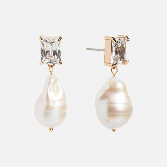 The Zeta Drop Earrings feature emerald-cut CZ stones framed in gold, each adorned with a dangling irregular white freshwater pearl, displayed on a white background.
