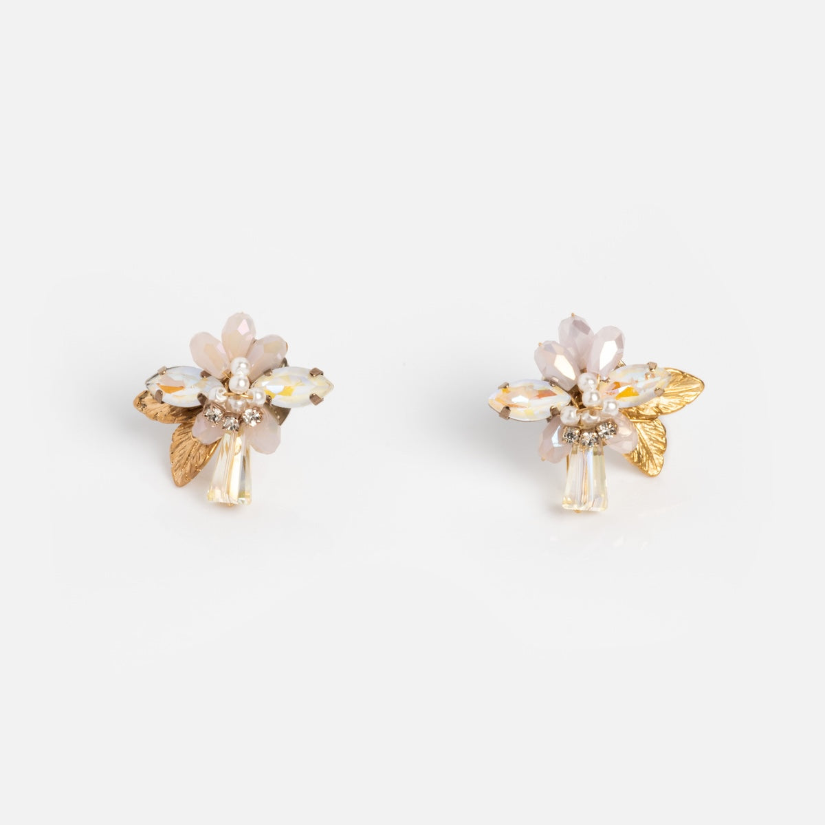 The Flora Crystal Cluster Earrings feature pale pink and white petals, 14k gold plated leaves, and sparkling crystals, displayed on a plain white background.