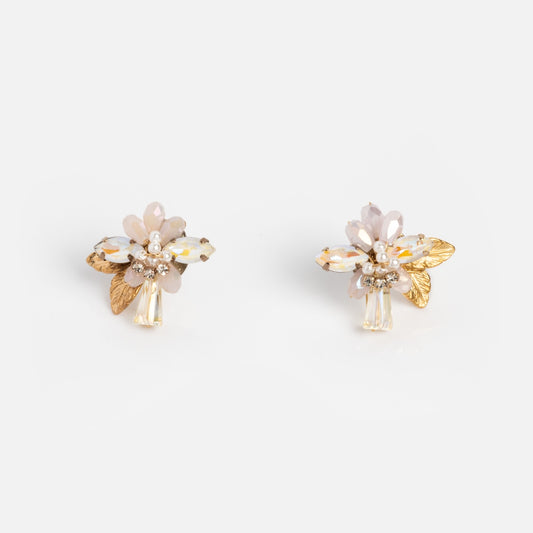 The Flora Crystal Cluster Earrings feature pale pink and white petals, 14k gold plated leaves, and sparkling crystals, displayed on a plain white background.