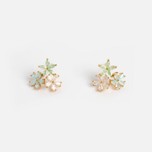 The Forget Me Not CZ Cluster Studs are 14k gold plated earrings featuring clusters of light green, pale blue, and clear petal-shaped stones delicately arranged as small flowers on a white background.