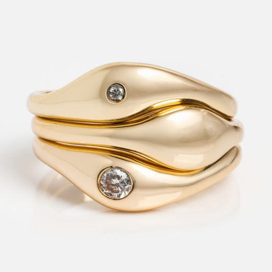 The Delphine Solitaire Ring Set in yellow gold showcases a wavy, layered design with two round diamonds nestled in its curves—an elegant and unique choice for those who love distinctive yellow gold rings.
