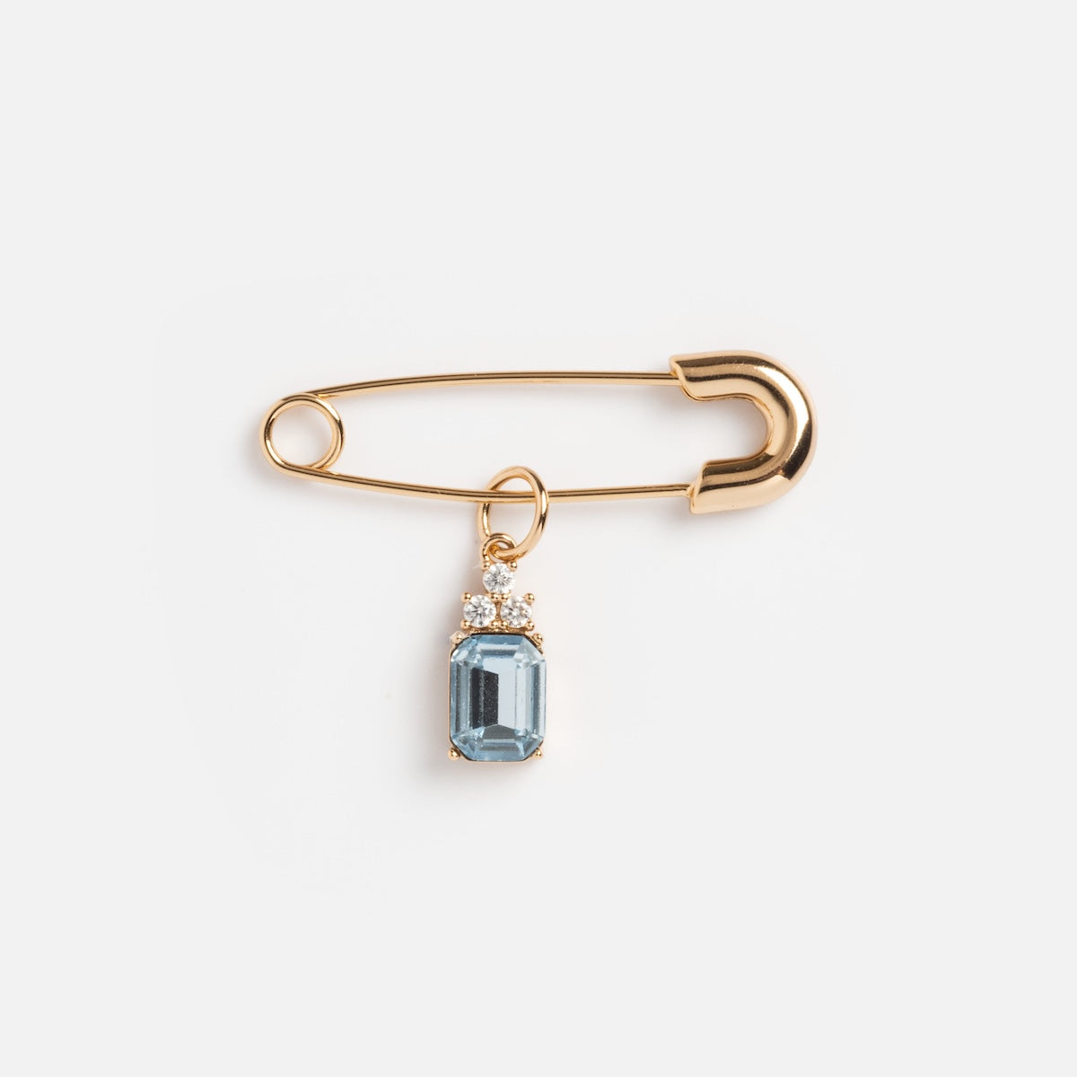 The Something Blue Pin features a gold safety pin with a blue gem charm and small clear stones pendant—an elegant bridal accessory—set against a plain white background.