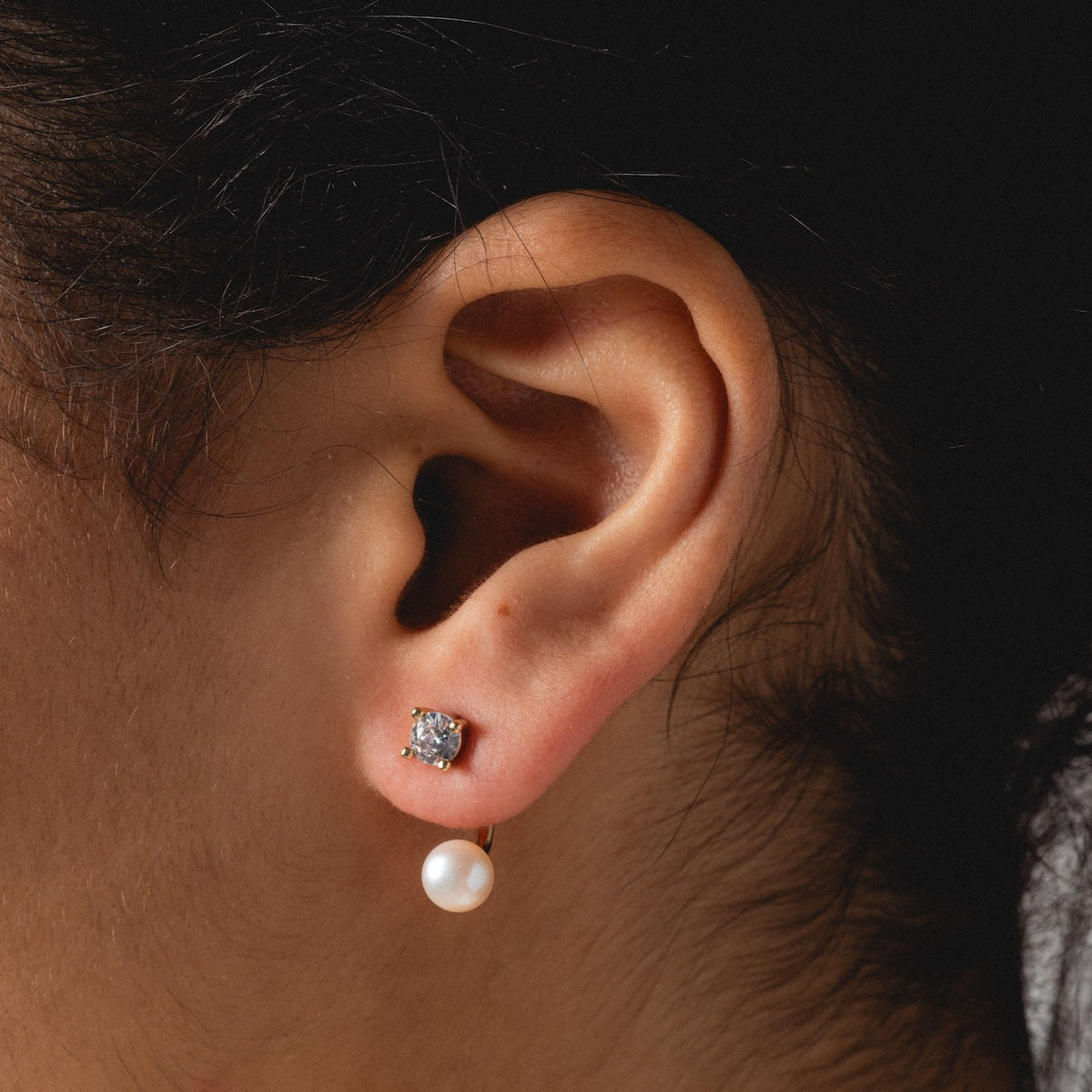 A close-up of a womans ear wearing the Aria Earrings—gold plated and accented with a delicate freshwater pearl.