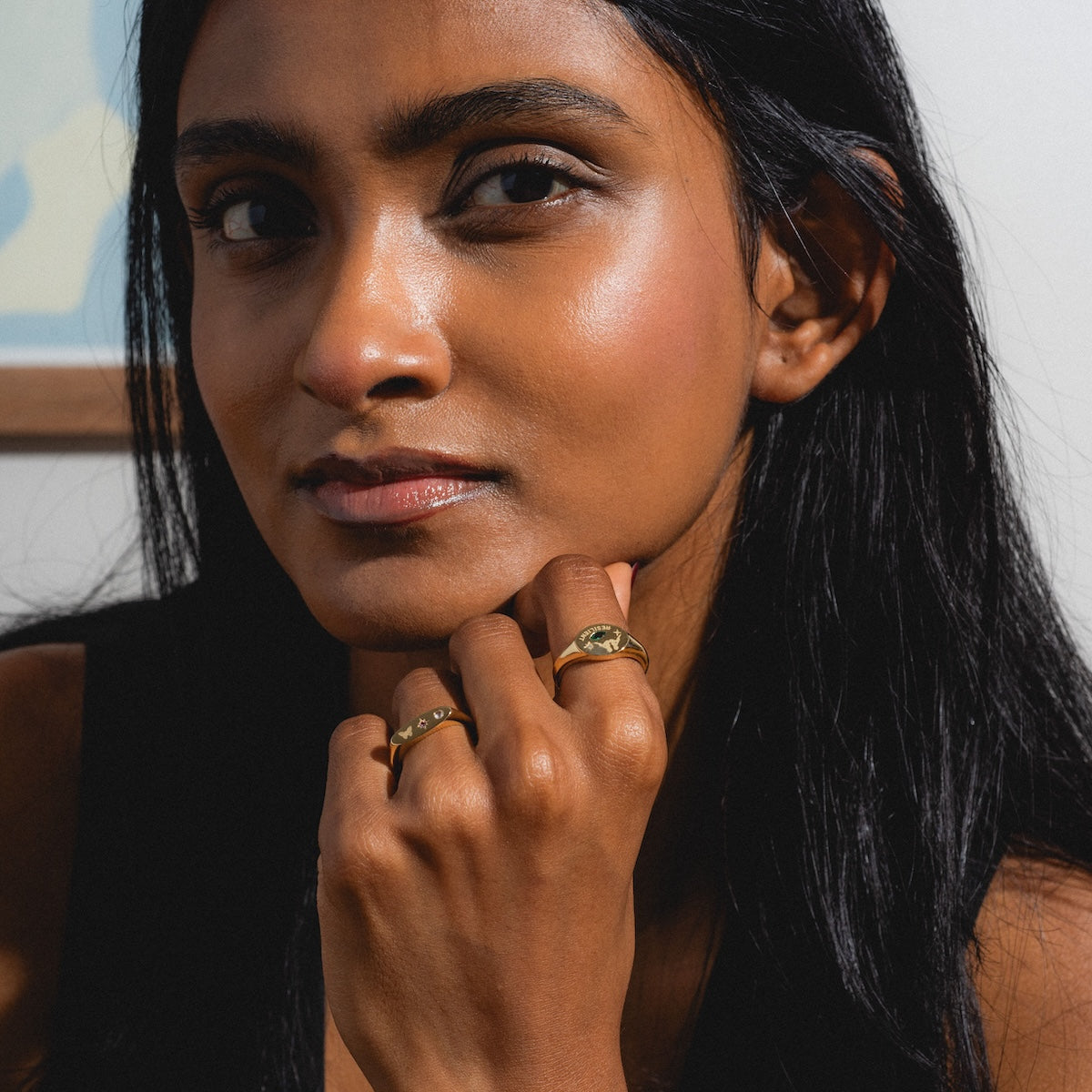 Woman with dark hair and rings on her fingers, wearing a black sleeveless top.