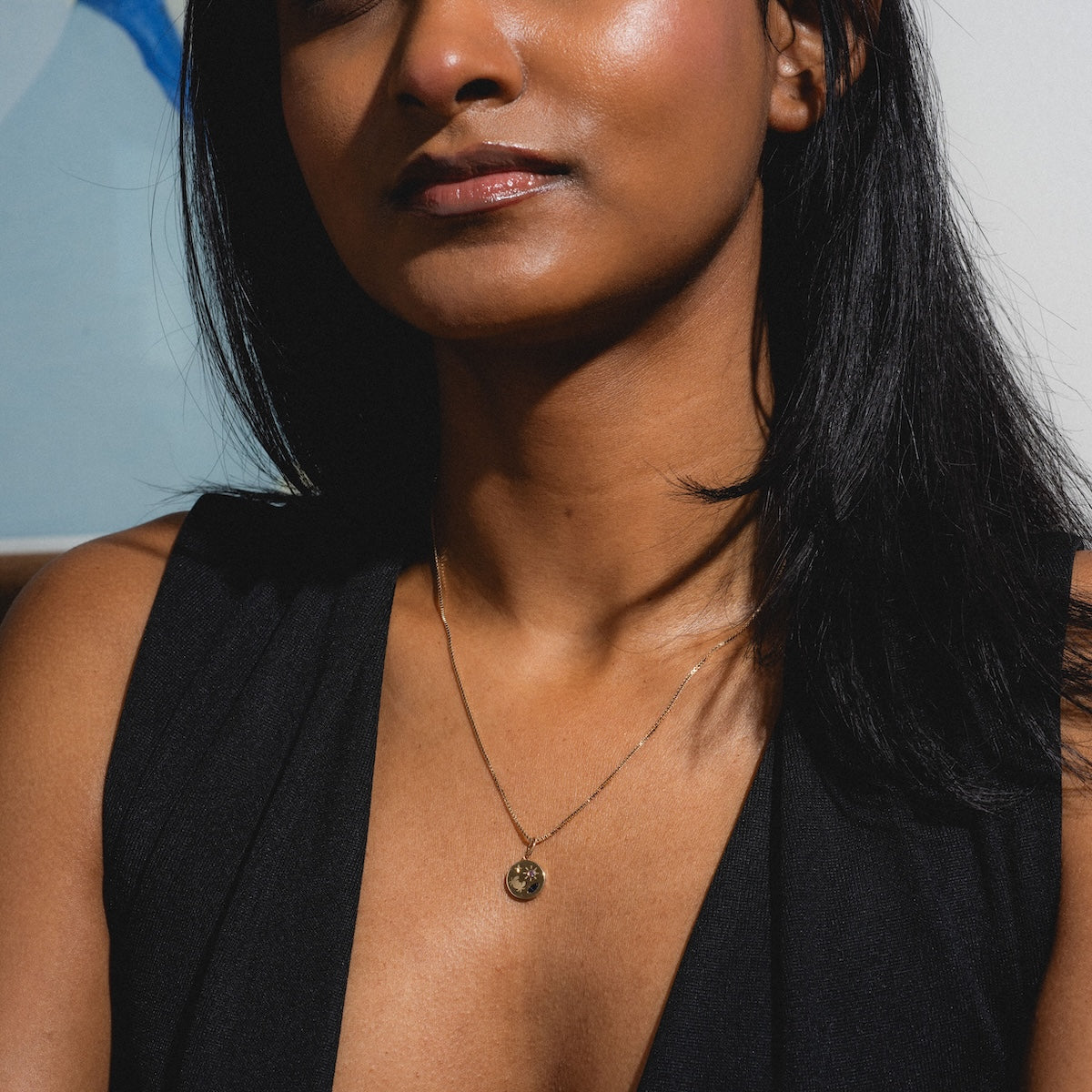 Woman wearing a necklace with a pendant against a neutral background