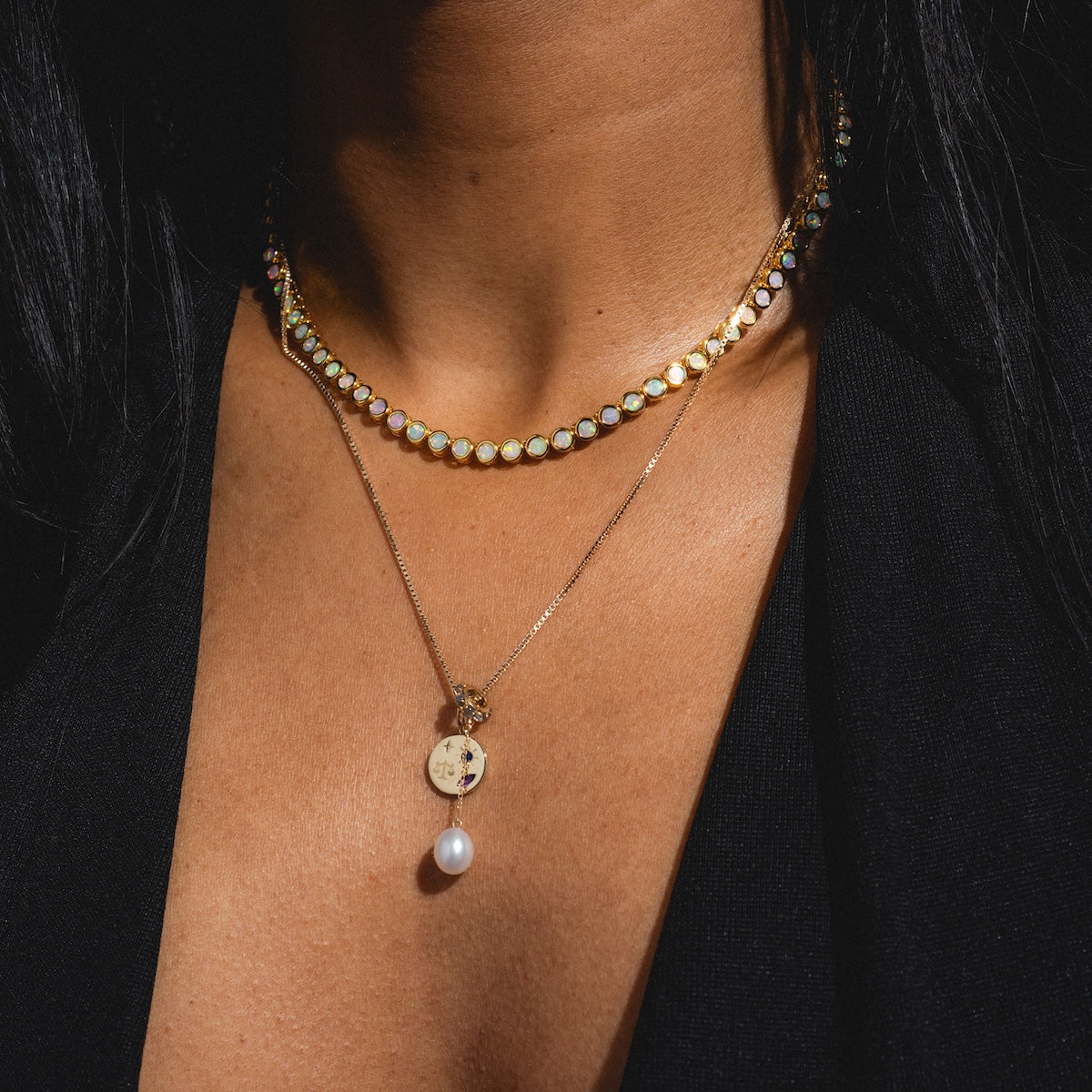 Close-up of a person wearing two necklaces with a black background