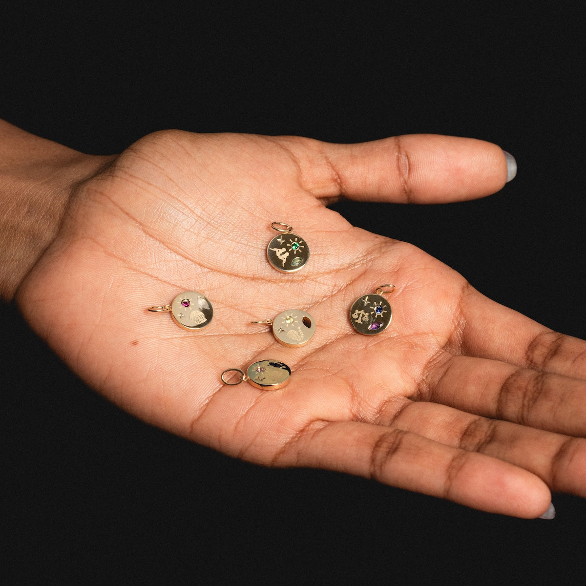 Hand holding small solid gold manifestation charms on a dark background
