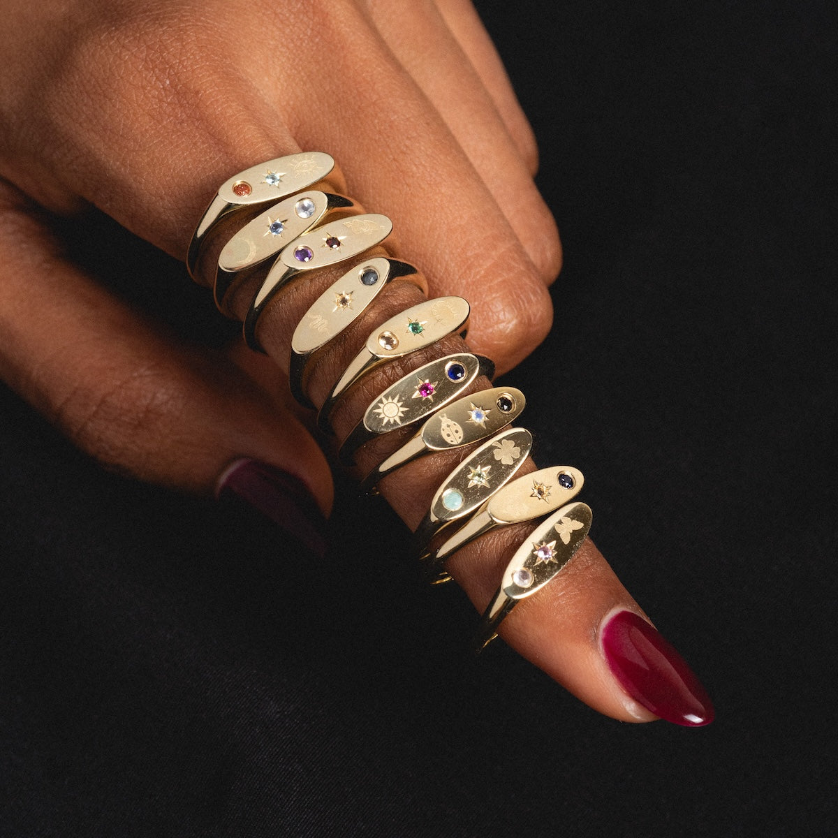 Gold manifestation rings with gemstones on a finger against a dark background