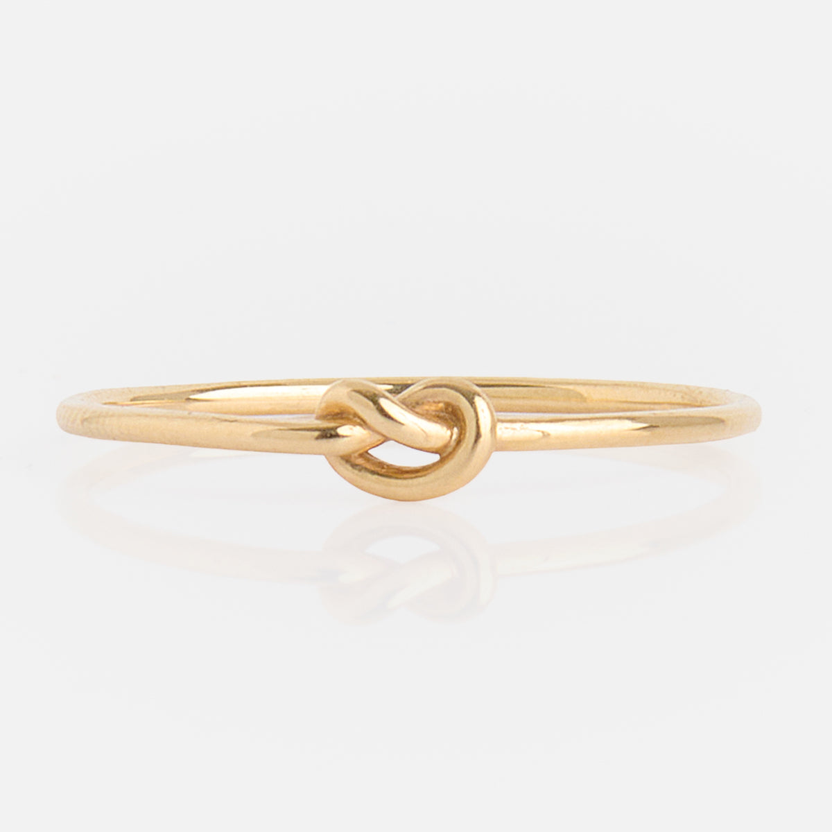 The Solid Gold Simple Knot Ring is a slender 10k yellow gold ring with a delicate knot centerpiece, showcased on a plain white background.