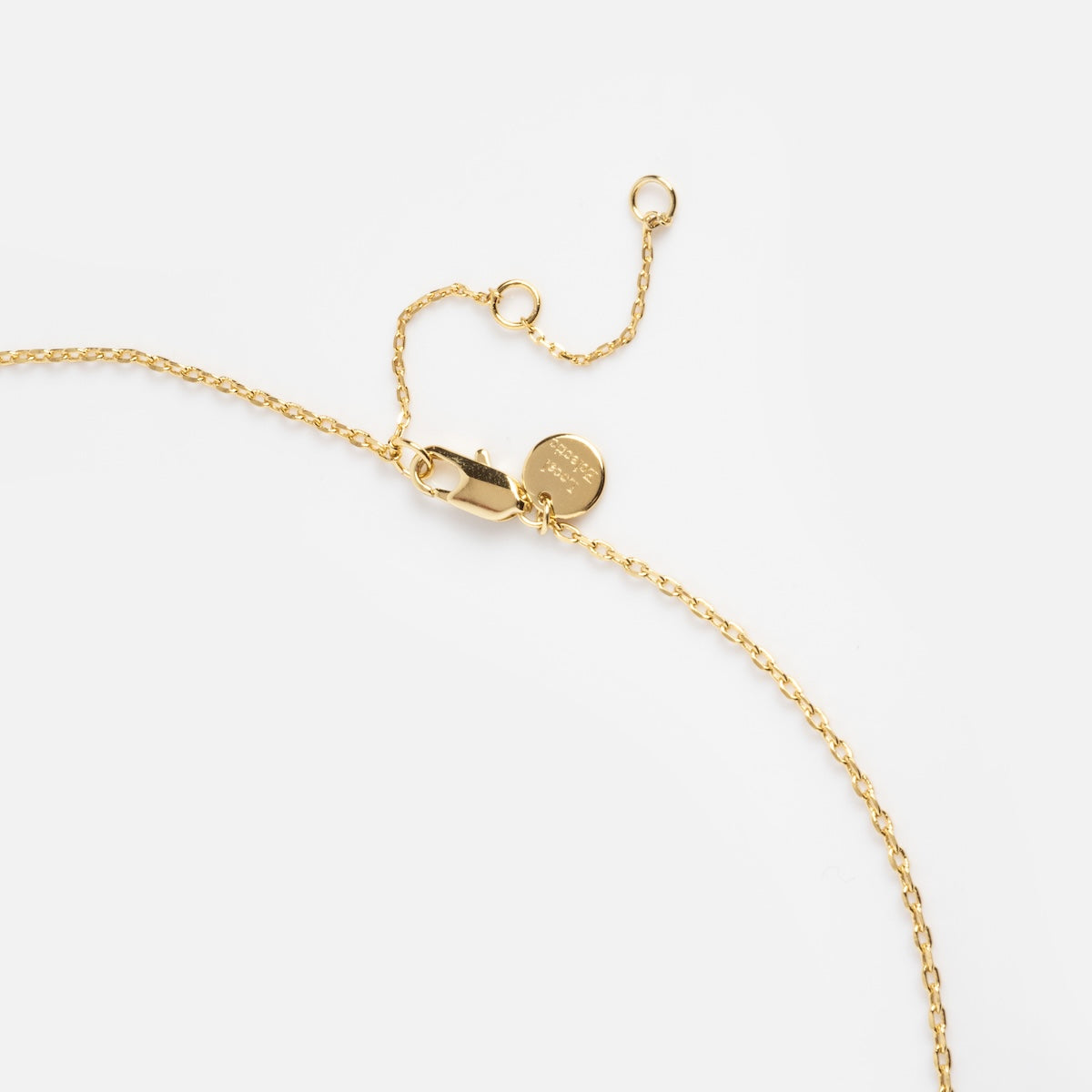 A close-up of the Oval Link Chain, a delicate gold plated necklace with oval links, a lobster clasp, an adjustable extension chain, and a small engraved round tag, displayed against a plain white background.