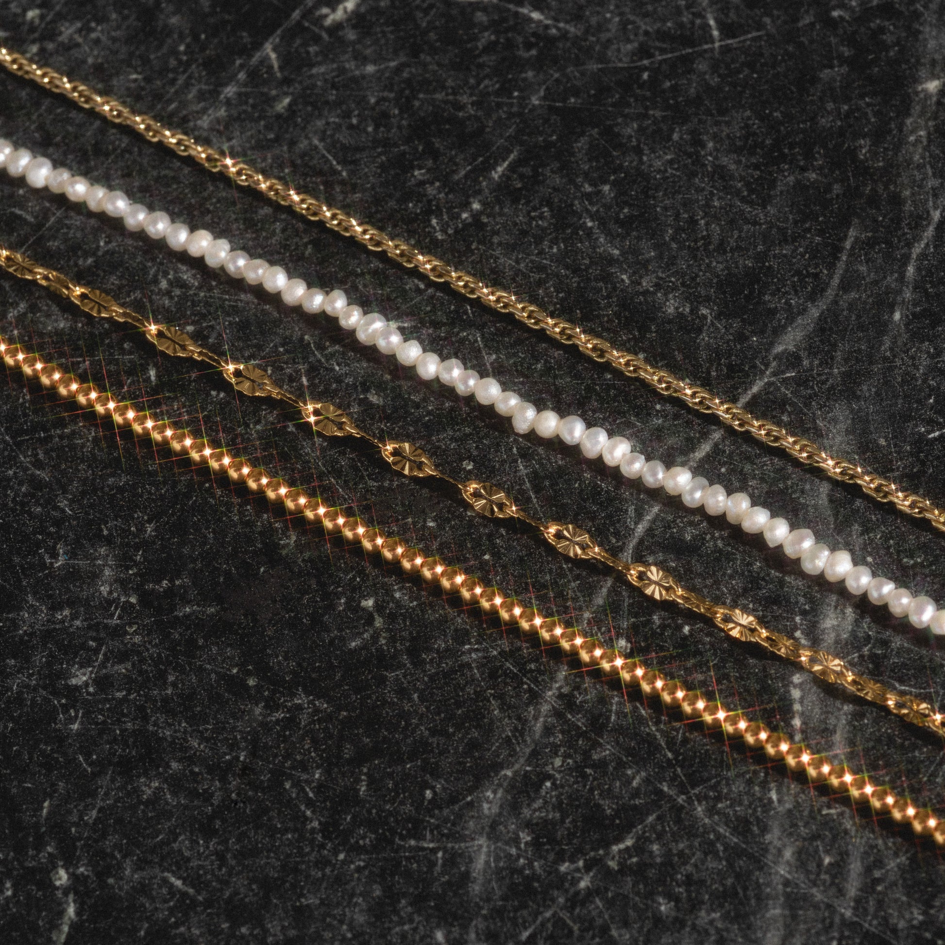 Delicate rope, beaded vermeil, pearl, and sparkle link chains on black marble