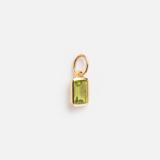 The Solid Gold Birthstone Baguette Charm August Sample is a small gold pendant with a rectangular, faceted green gemstone and an attached gold loop, displayed on a plain white background.