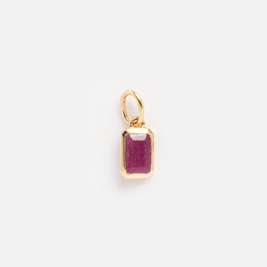 The Solid Gold Birthstone Baguette Charm July Sample features a rectangular, faceted deep pink gemstone in a gold frame with a loop for chains, shown on a plain white background.