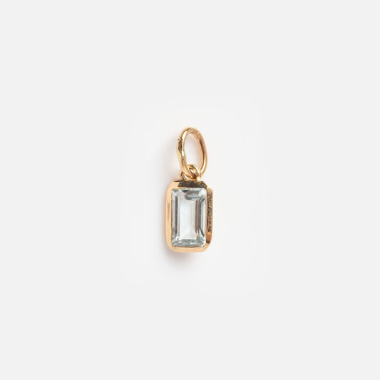 The Solid Gold Birthstone Baguette Charm March Sample is a small gold pendant with a rectangular clear gemstone in a simple gold frame and loop, shown on a plain white background.