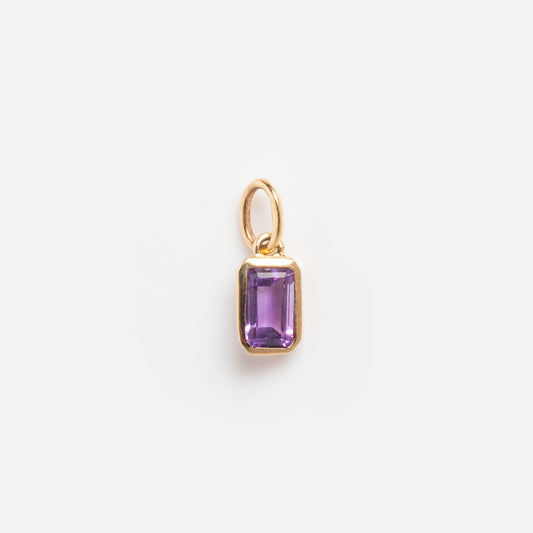The Solid Gold Birthstone Baguette Charm February Sample features a small rectangular purple gemstone set in a gold frame with a gold loop, shown against a plain white background.