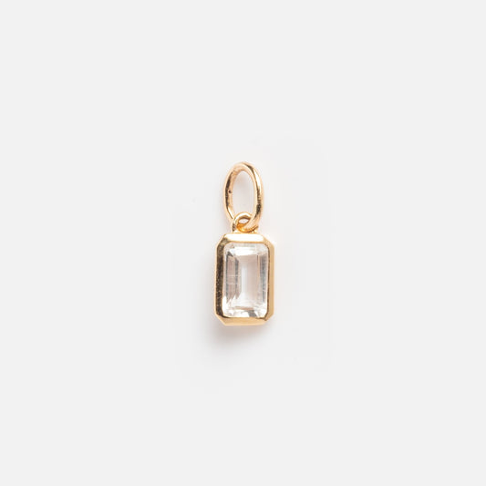 The Solid Gold Birthstone Baguette Charm April Sample features a rectangular clear gemstone in a gold bezel with a small gold loop, shown against a plain white background.