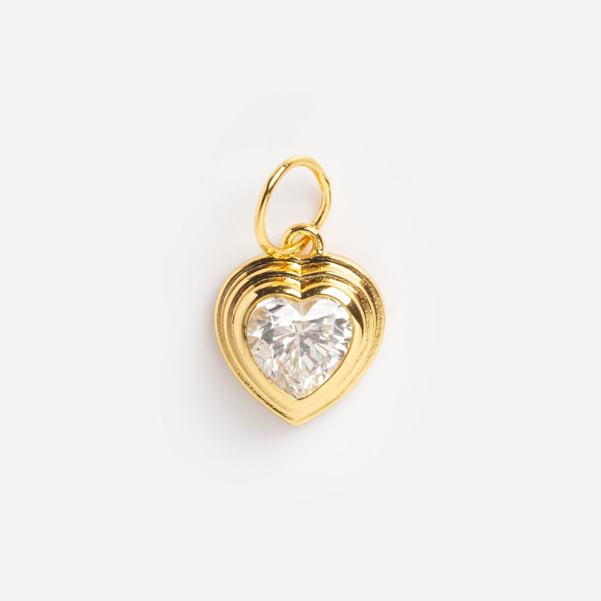 The Charms by Jurate JLA is a yellow gold plated, heart-shaped pendant with a layered border and a large, faceted clear gemstone at its center, showcased elegantly on a plain white background.