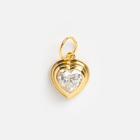 The Charms by Jurate JLA is a yellow gold plated, heart-shaped pendant with a layered border and a large, faceted clear gemstone at its center, showcased elegantly on a plain white background.