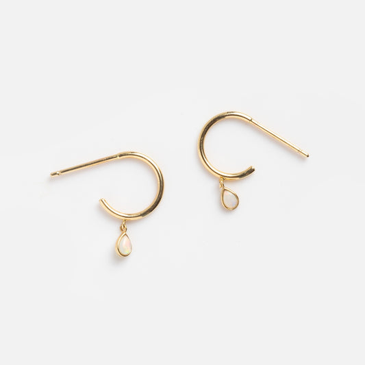 The Solid Gold Teardrop Opal Huggie Earrings Sample features small gold hoops with delicate teardrop opal charms, shown against a plain light gray background.
