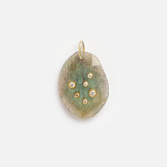 The Labradorite Libra Constellation Charm Sample is an oval pendant with a greenish, textured surface, adorned with seven round gold and diamond-like studs in a scattered pattern, and finished with a small gold loop at the top.