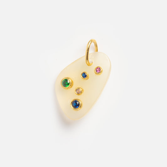 The White Chalcedony Cancer Constellation Charm Sample is a small, irregularly shaped pale yellow pendant with a gold loop and five embedded gemstones in green, blue, pink, and clear on its surface.