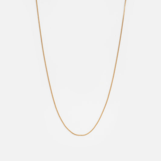 The Solid Gold Delicate Curb Chain Sample, a simple and thin gold necklace, is elegantly displayed against a plain white background.
