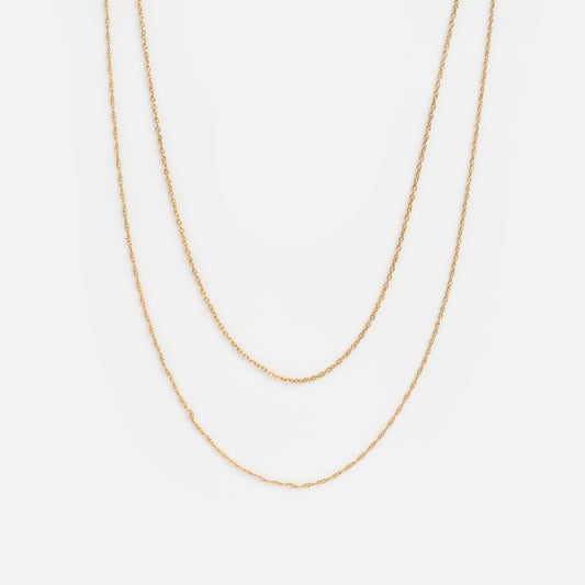 The Solid Gold Delicate Double Layered Necklace Sample features two elegant gold chains of varying lengths, showcased on a plain white background.
