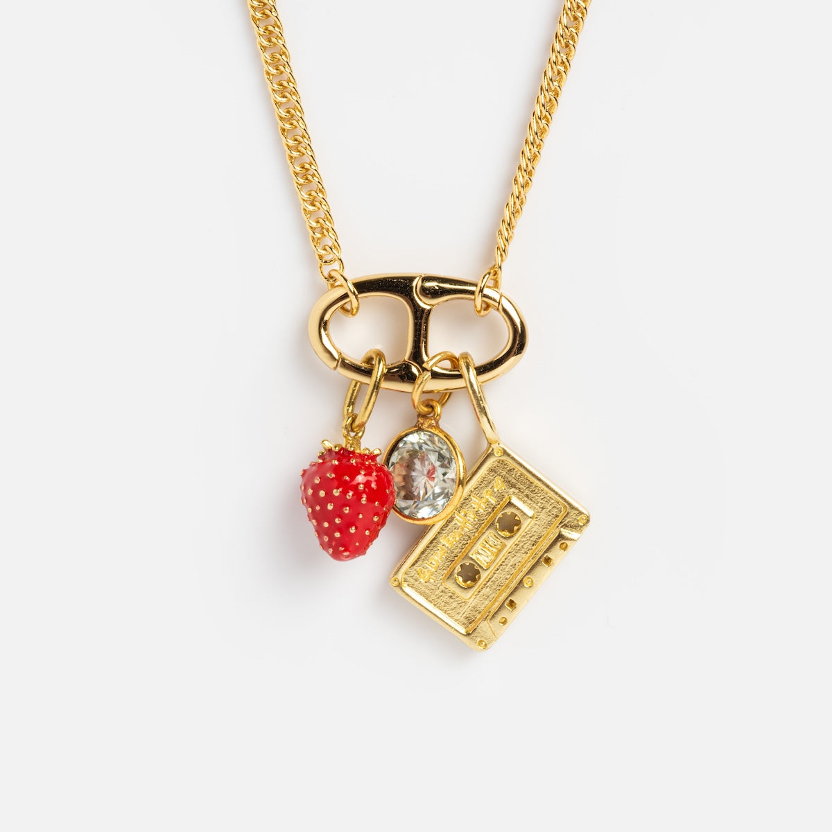 The Perfect Start Charm Holder Necklace features a gold plated chain with three playful charms—a red strawberry, a clear oval gem, and a gold cassette tape—shown on a white background.