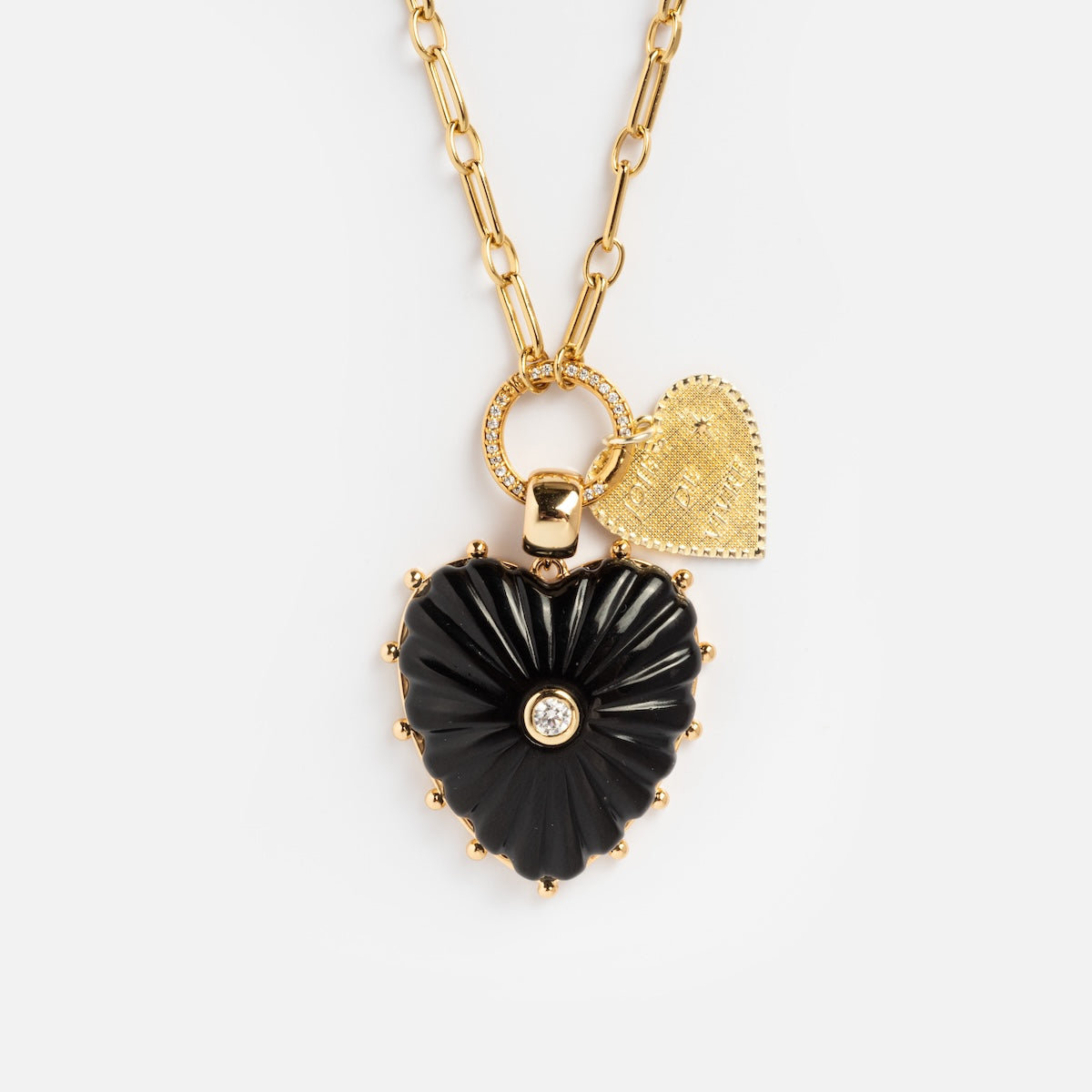 The Perfect Start Charm Holder Necklace features a gold-plated chain with two heart pendants: one black with a central gem, the other textured gold with an engraved pattern—an elegant and versatile accessory.
