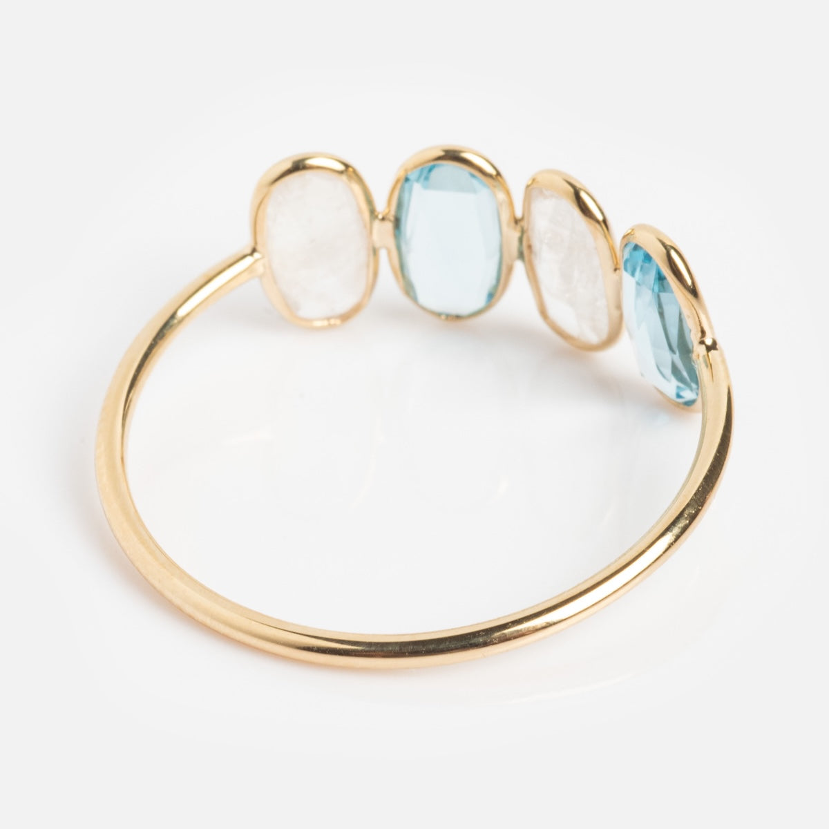 The Solid Gold Daybreak Moonstone and Blue Topaz Ring in 9k yellow gold features two oval moonstones and two oval blue topaz gems set side by side, making it a unique choice for a striking gemstone ring.