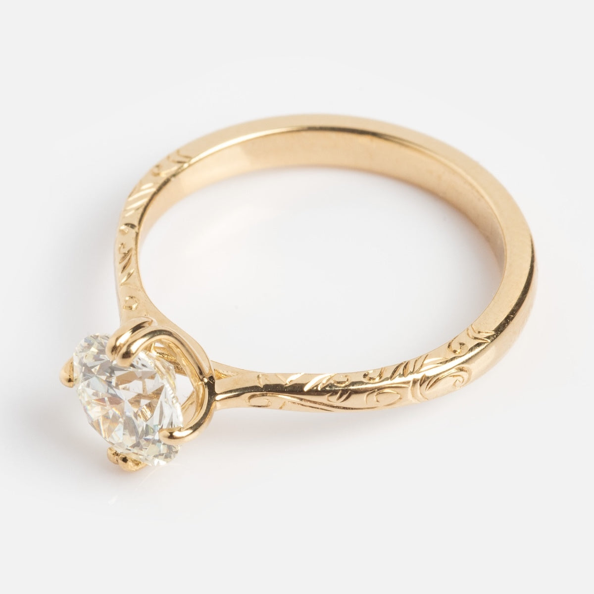 A Bespoke Design Consultation for a gold engagement ring with a round diamond solitaire and engraved floral band, ideal for those seeking custom jewelry, shown on a white background.