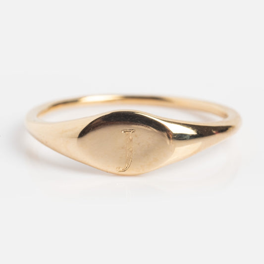 The Solid Gold Engravable Simple Signet Ring J Sample Size 6 is a 9k yellow gold ring with a smooth oval face and an engraved J in the center, shown against a plain white background.