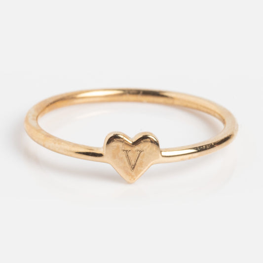 The Solid Gold Engravable Heart Ring V Sample is a 9k yellow gold ring with a central heart detail engraved with the letter V, shown on a plain white background.
