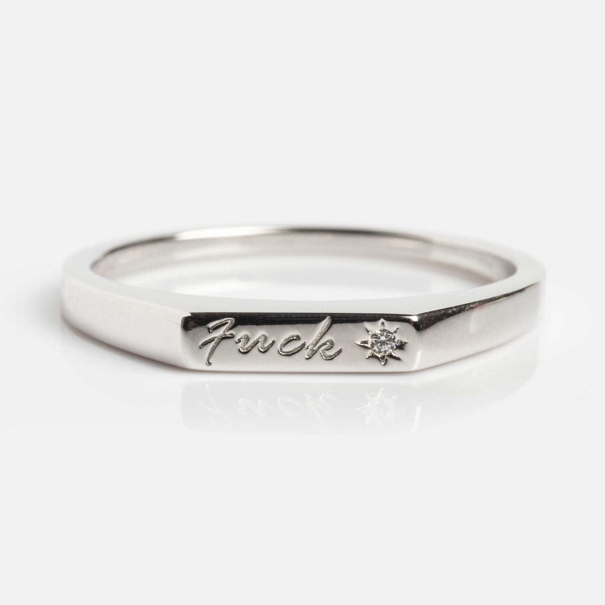 The Tiny Fuck Ring features "fuck" engraving and a star with a tiny gemstone in 14k yellow gold plating. Available exclusively at Local Eclectic, it's shown against a plain white background.