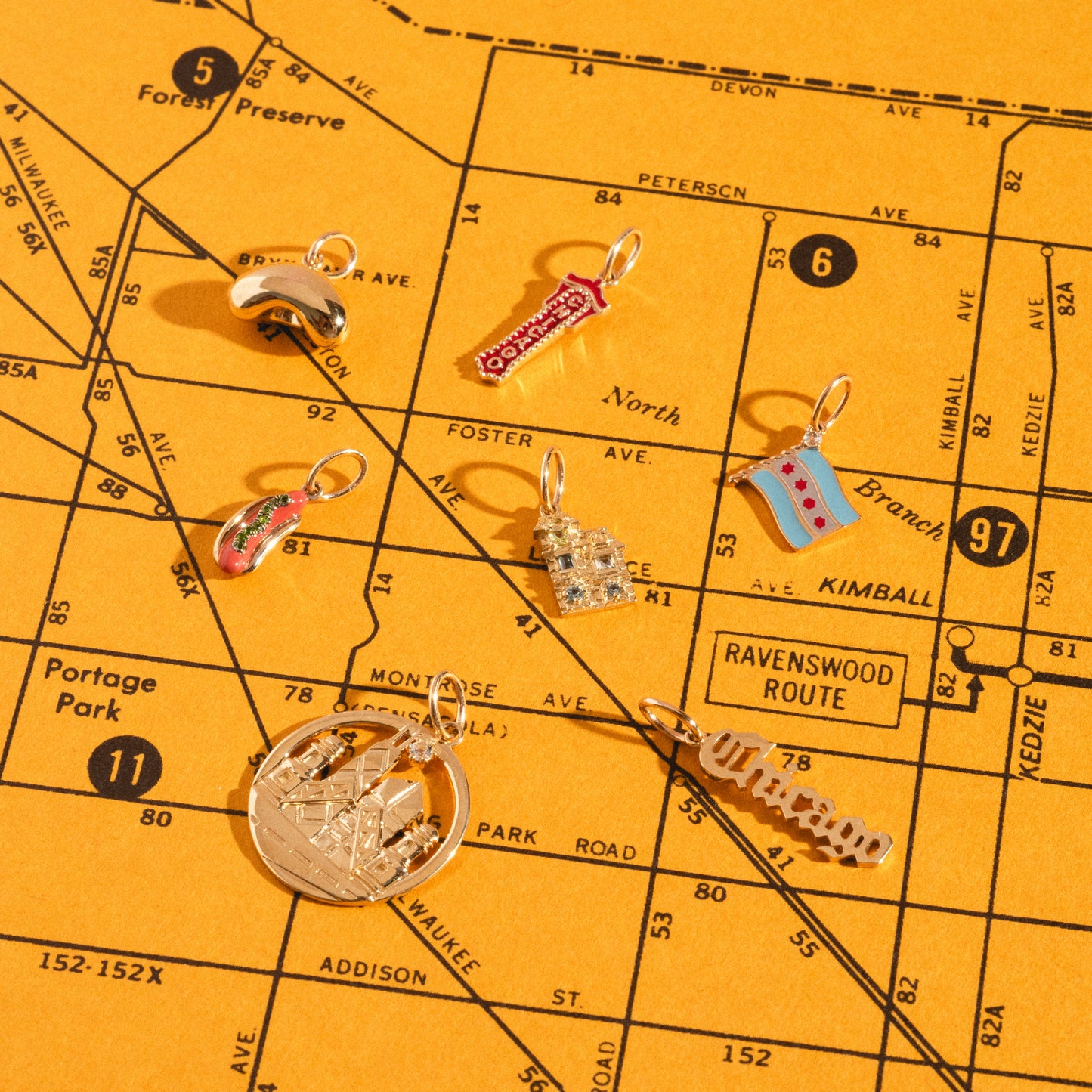 The Solid Gold Chicago Charms, shaped like city icons, are displayed on a vintage yellow map of Chicago featuring street and neighborhood names such as Portage Park and Ravenswood Route.