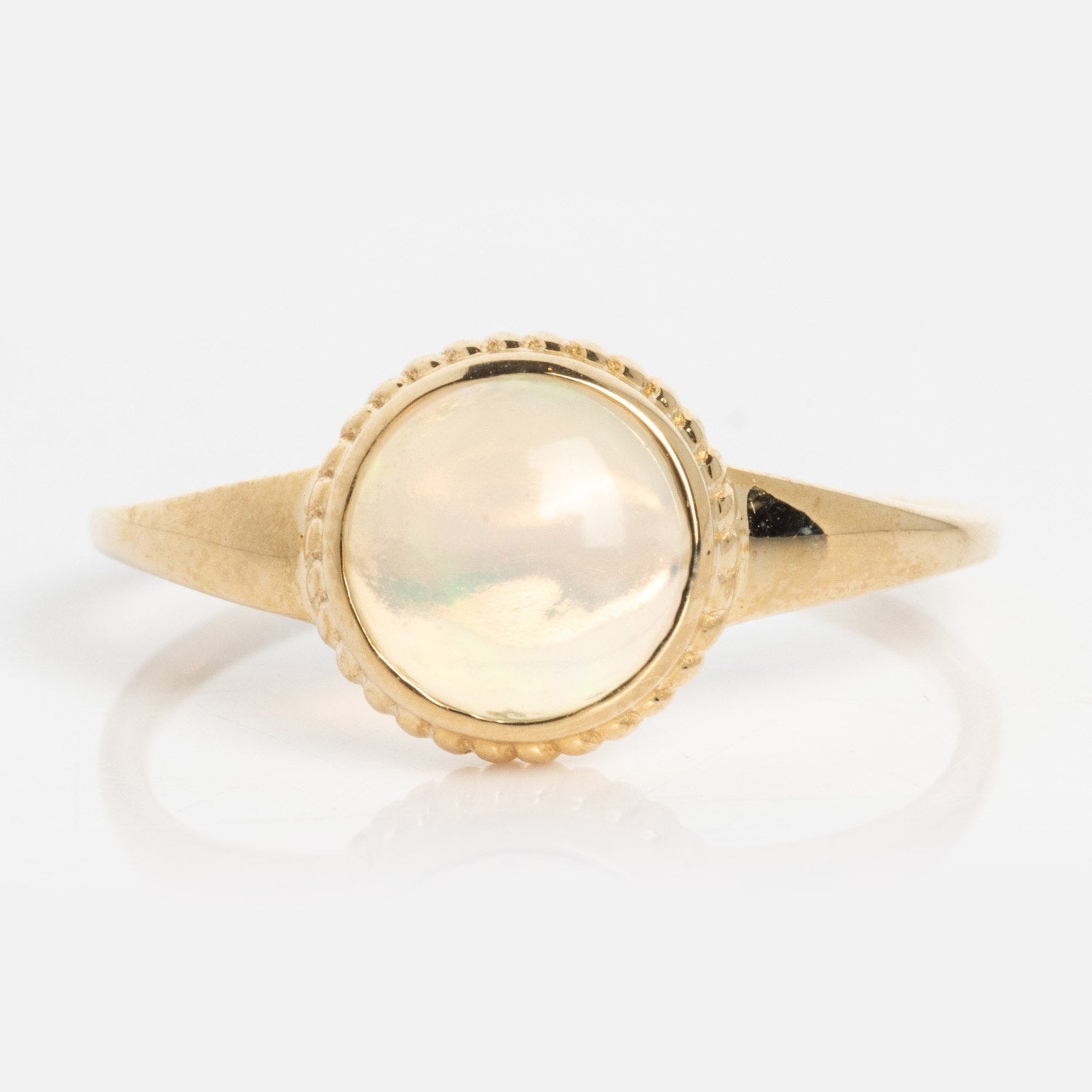 The Solid Gold Textured Opal Signet Ring showcases a round, iridescent opal set in a textured bezel on a polished gold band, displayed on a light background.