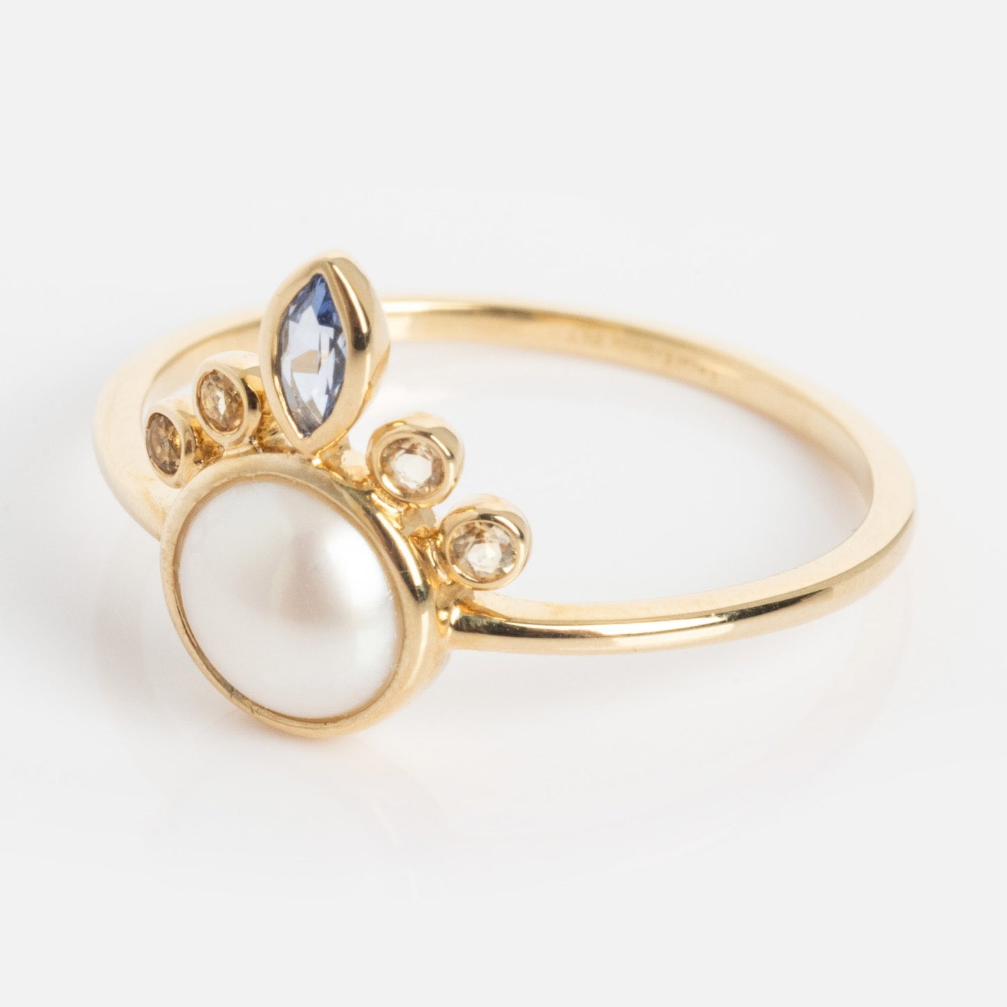 The Solid Gold Crowned Bezel Pearl Ring showcases a prominent round pearl centerpiece with three small round gemstones and a marquise-shaped clear stone clustered decoratively on one side of the band.
