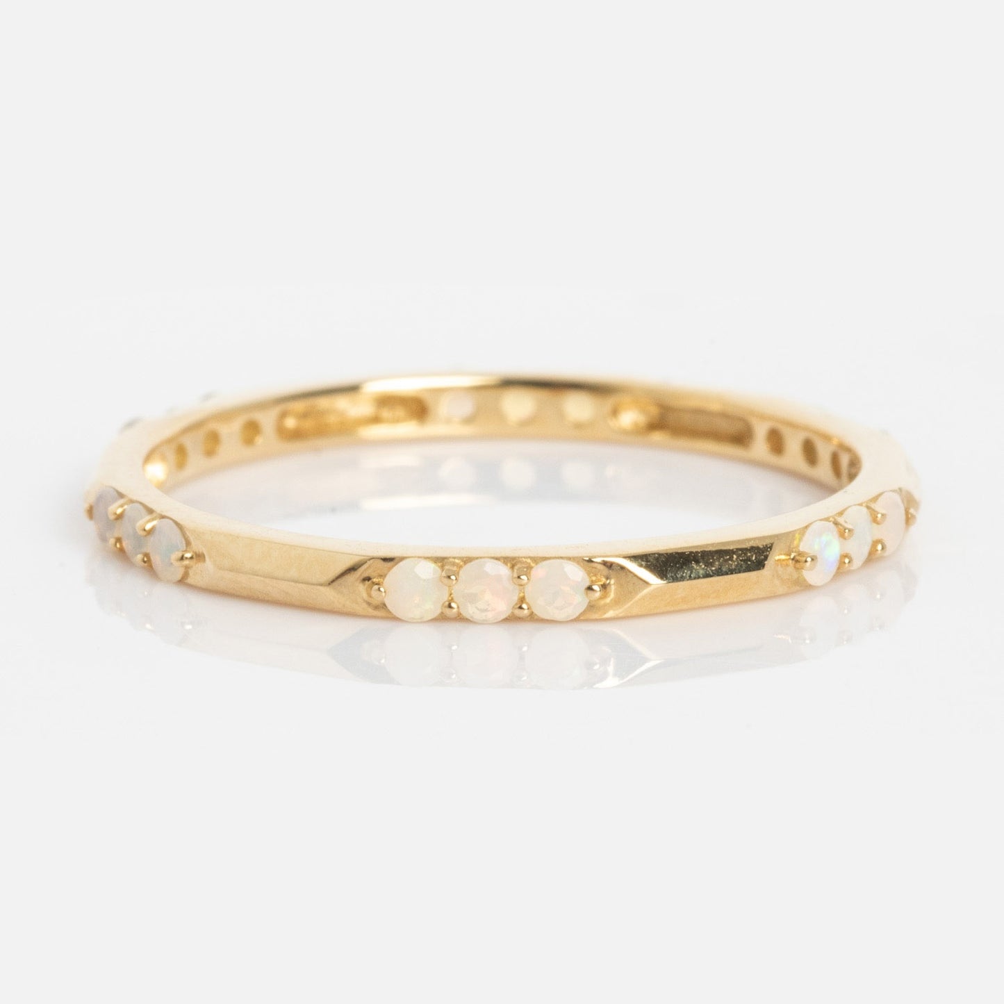 The Solid Gold Beveled Opal Stacking Ring features small round opal stones evenly spaced around its thin gold band, shown on a plain white background.