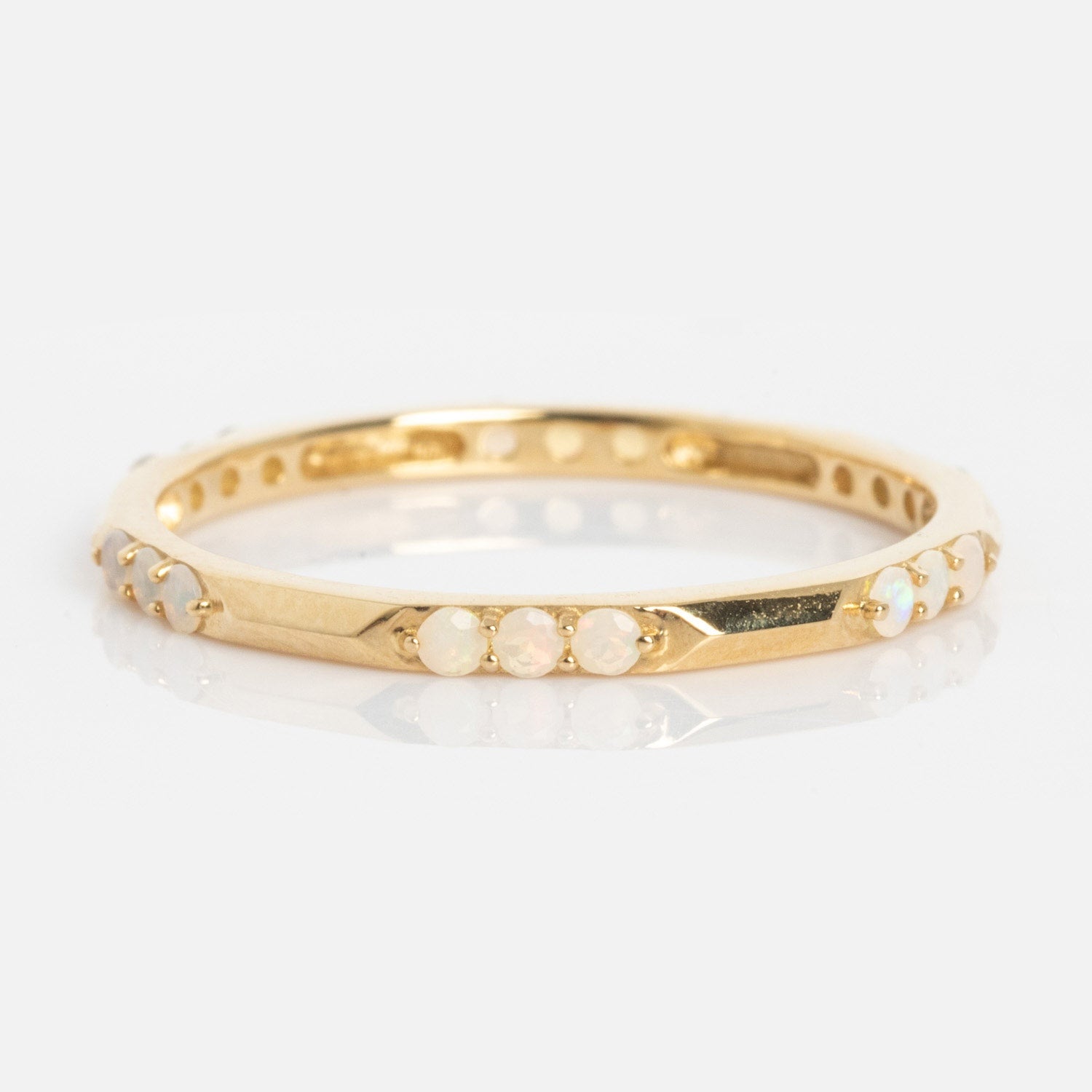 The Solid Gold Beveled Opal Stacking Ring features small round opal stones evenly spaced around its thin gold band, shown on a plain white background.